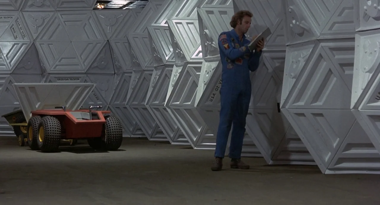 Silent Running (1972) movie still: fullbody — A spacious interior room features walls constructed of modular white hexagonal geometric panels. A man…
