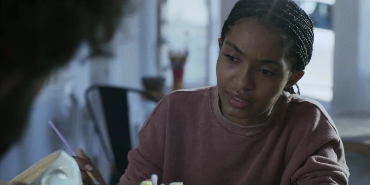 Sitting in Bars with Cake (2023) movie still: medium — A light-filled room contains a young woman and an out-of-focus subject nearby. The woman in…