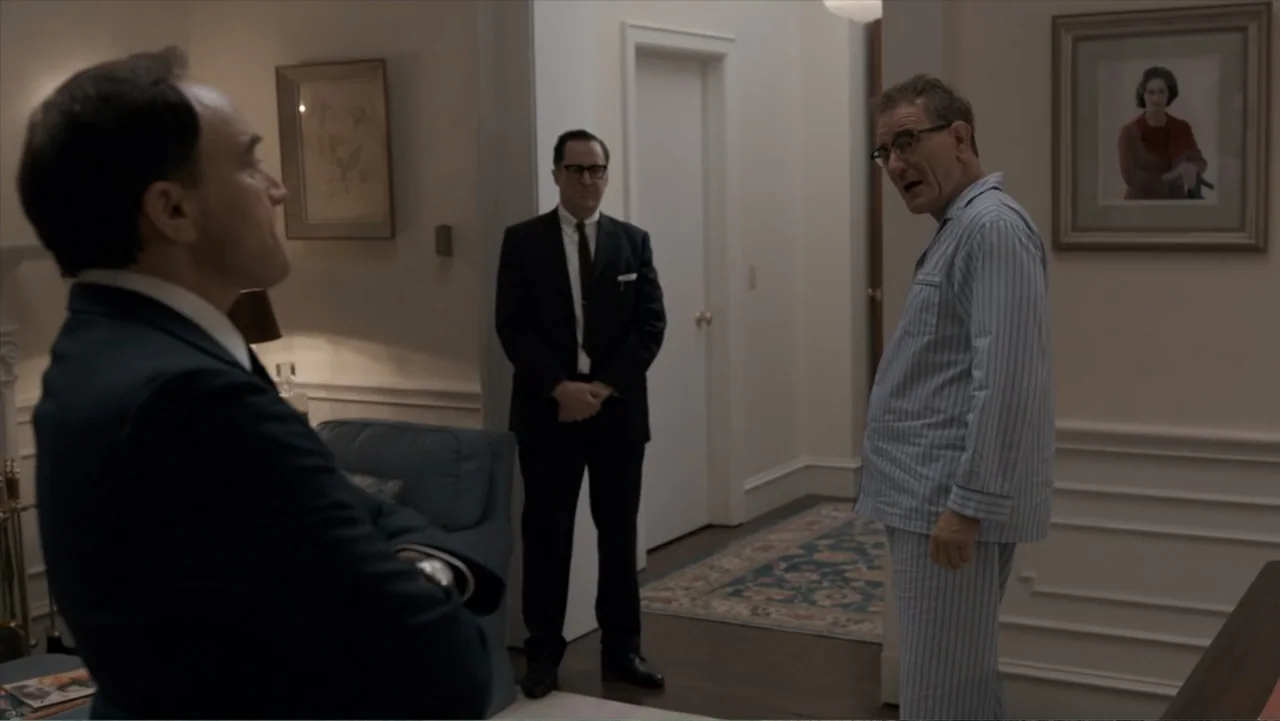 All the Way (2016) movie still: medium — A well-appointed 1960s living room features framed portraits on cream-colored walls. Two men in business…