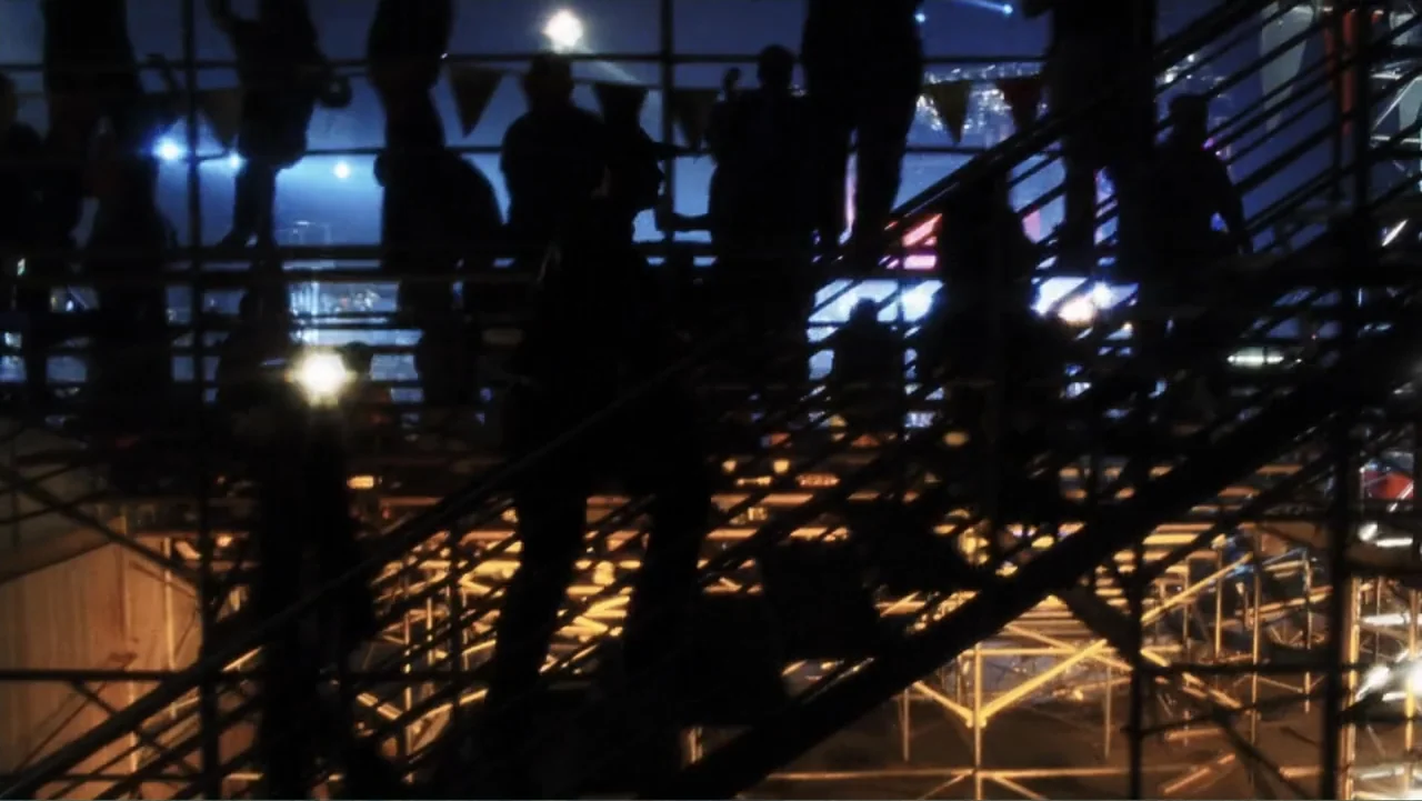 A.I. Artificial Intelligence (2001) movie still: wide — A dense crowd of people ascends metal bleacher stairs under bright stadium floodlights at…