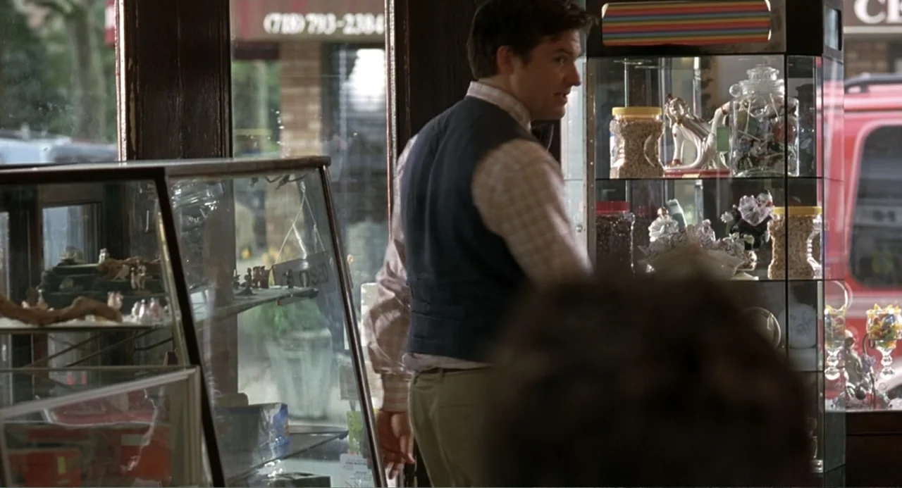 Mi Perfecto Ex (2024) movie still: medium — A cluttered candy shop interior features glass display cases filled with assorted sweets and trinkets. A…