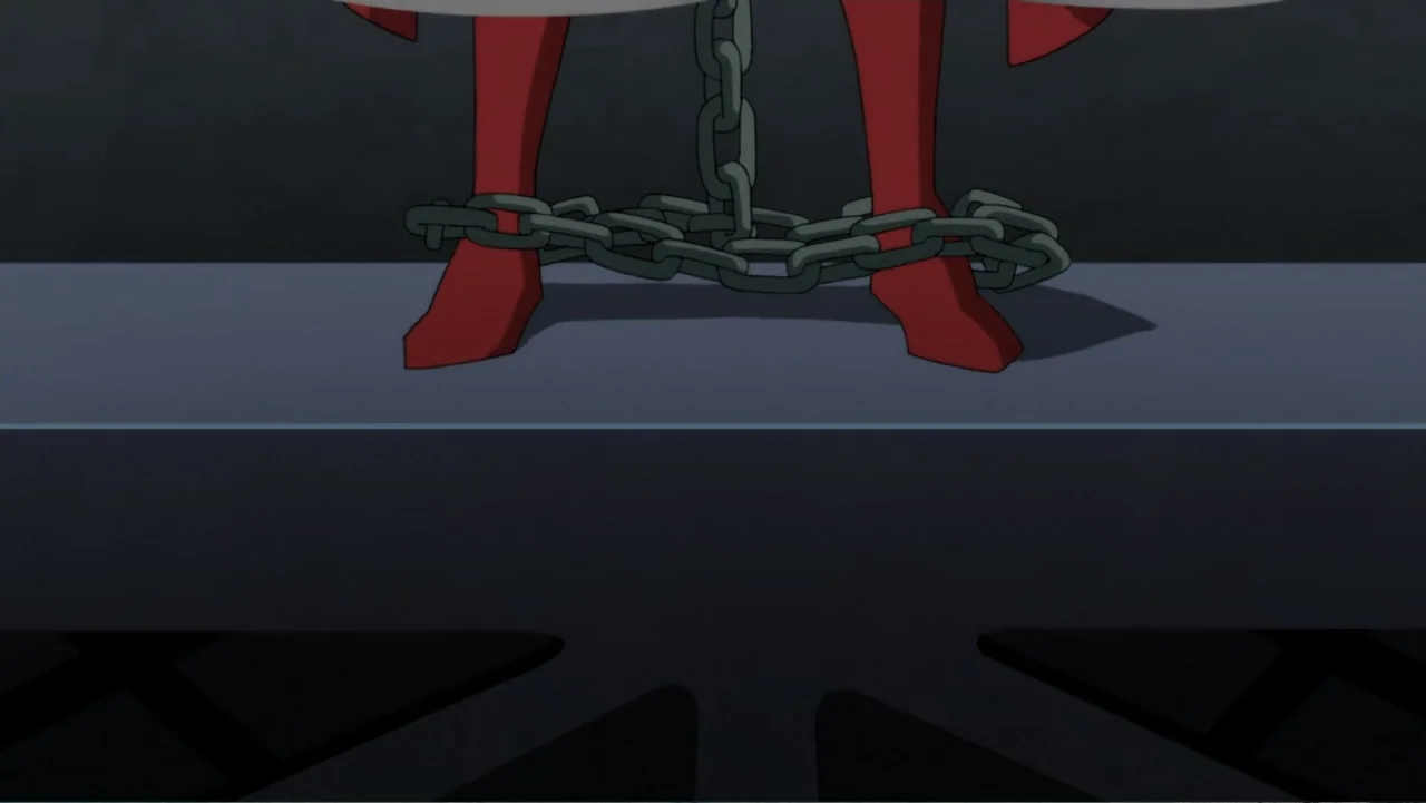 Superman: Red Son (2020) movie still: closeup — A dark, spartan interior environment features a flat metallic surface against a grey wall. Heavy…