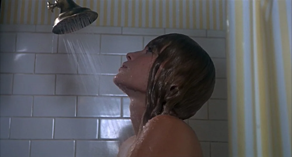 Rosemary’s Baby (1968) movie still: medium — A tiled stall with a classic metallic showerhead and light-colored vertical striped wallpaper. A woman…