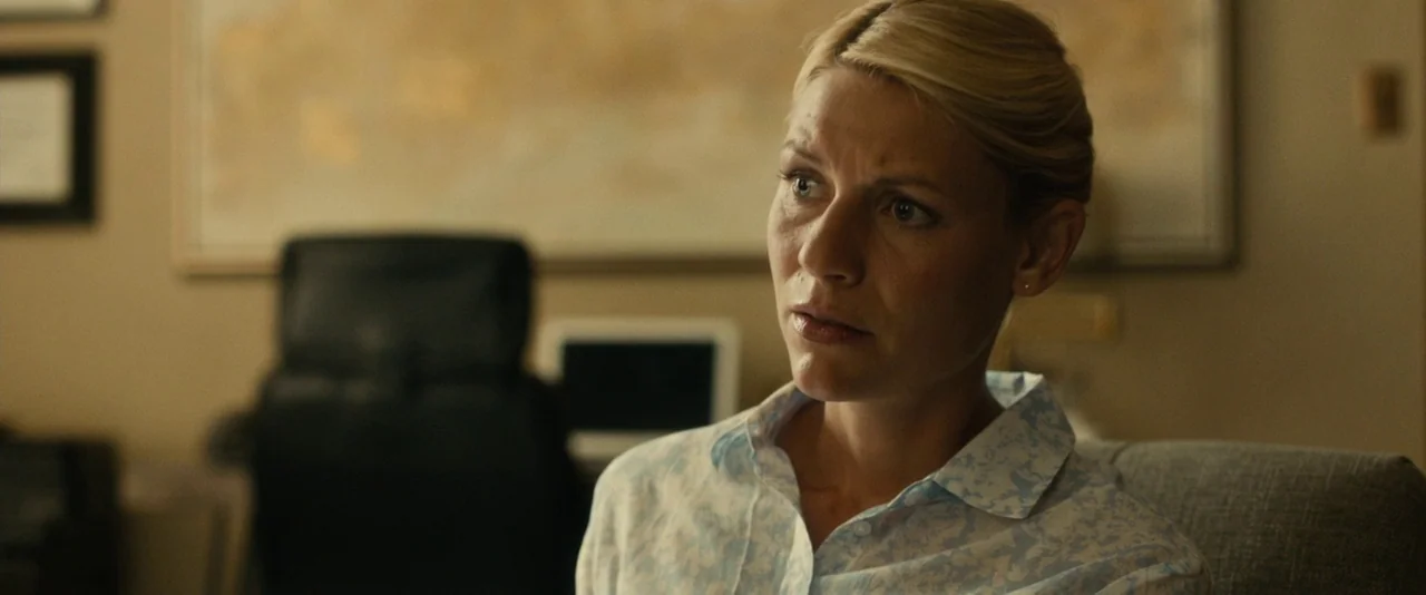 Brigsby Bear (2017) movie still: medium — A professional space features a blurred desk and a large map on the wall. A woman with blonde hair sits in…
