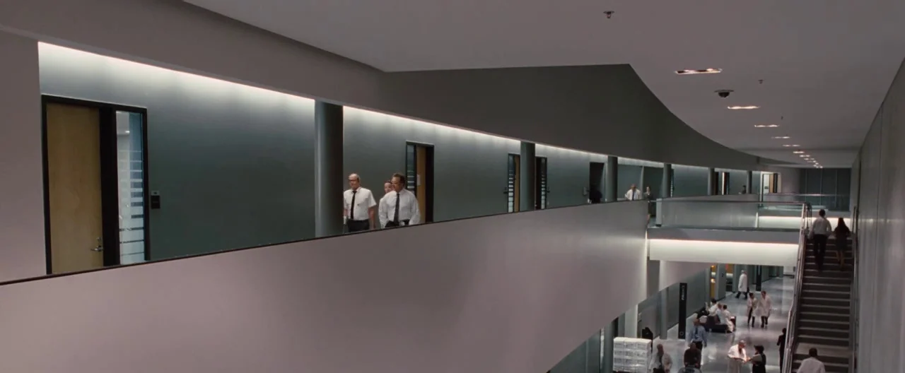 The Cabin In The Woods (2012) movie still: wide — A modern two-story office corridor features clean concrete walls, glass railings, and recessed…