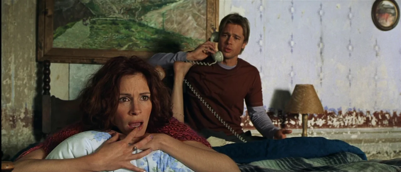 The Mexican (2001) movie still: medium — A distressed room features peeling light blue wallpaper and a large landscape painting above. A man sits on…
