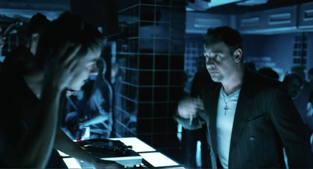 Soul Kitchen (2009) movie still: medium — A dimly lit nightclub features tiled dark walls and a brightly glowing rectangular DJ desk. A man in a…