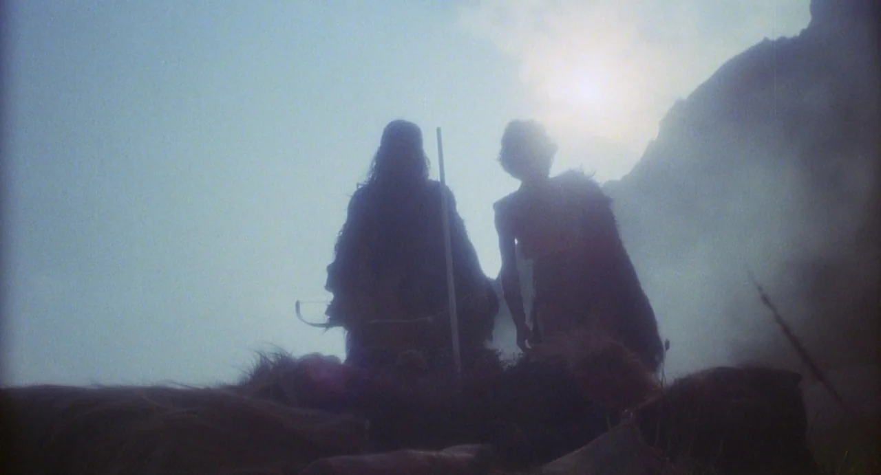 Conquest (1983) movie still: fullbody — A misty, rugged mountain landscape bathed in bright sunlight from above. Two figures stand close together as…