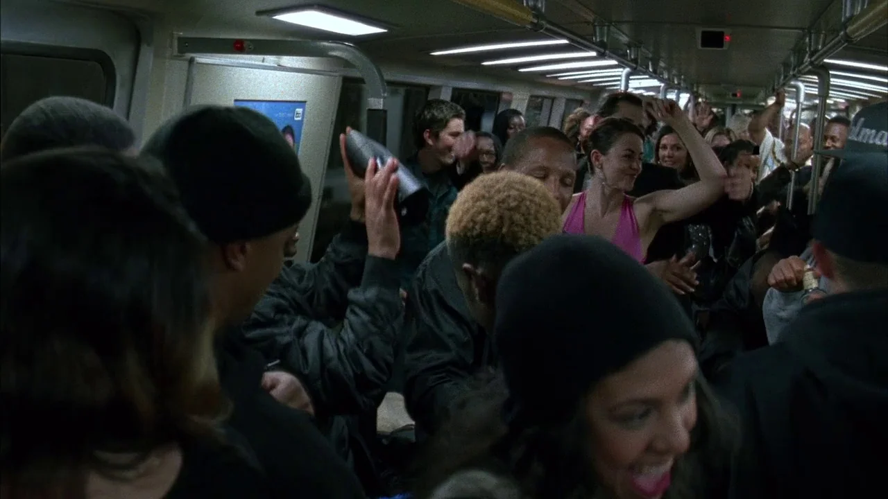 Fruitvale Station (2013) movie still: medium — An interior shot of a packed commuter train car filled with standing passengers. Multiple people are…
