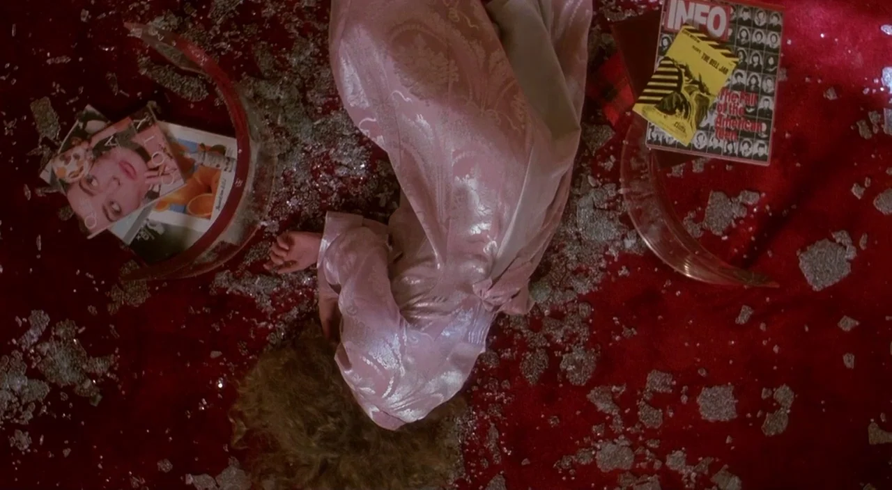 Heathers movie still: medium — A floor covered in a vibrant red carpet scattered with fragments of shattered glass. A person in a pink satin…