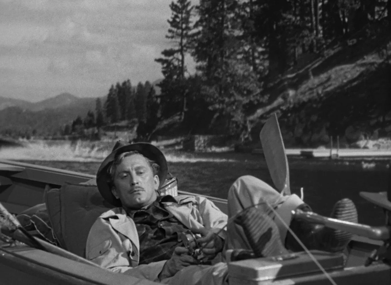 The Bad and the Beautiful (1952) movie still: medium — A man lies in a wooden rowboat on a lake surrounded by evergreen trees. He reclines against…