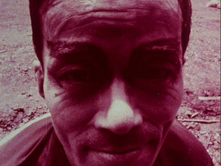 Emperor Tomato Ketchup movie still: closeup — A close-up shot focuses on a person's face against a coarse, textured dirt background. The subject…