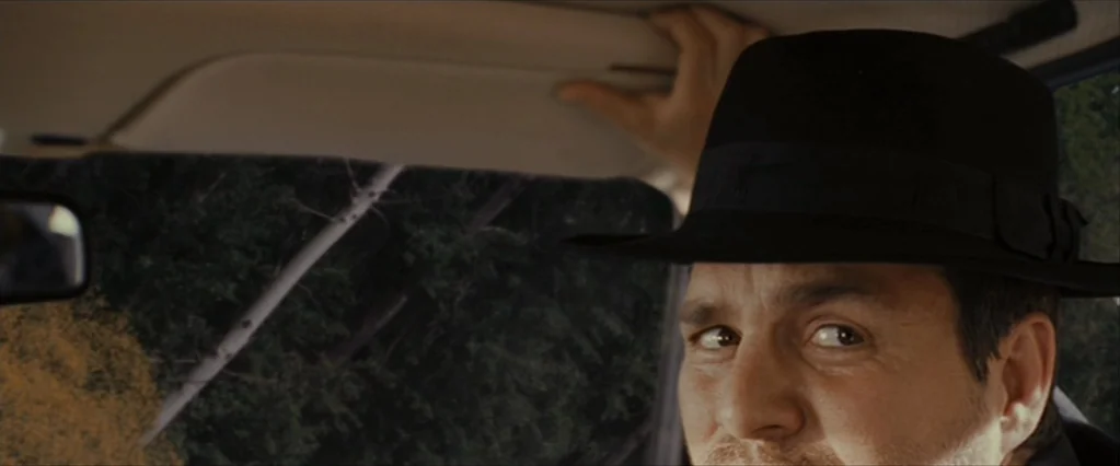 The Brothers Bloom (2008) movie still: closeup — A view from inside a car looking toward the driver seat. The man glances out the window while…