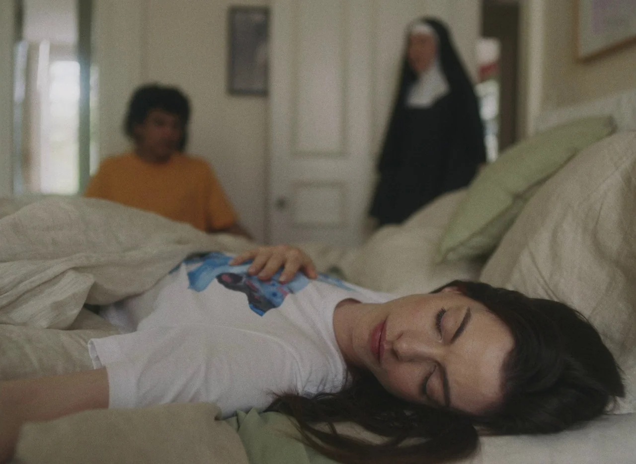 She Came To Me (2023) movie still: medium — A bright domestic interior with neutral walls and a rumpled white duvet on the bed. A woman sleeps while…