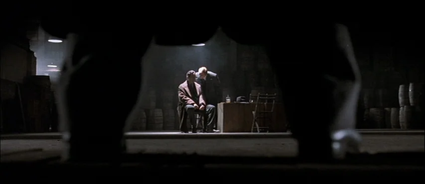 Road To Perdition (2002) movie still: wide — A dark subterranean space is filled with stacks of barrels and industrial fixtures. Two men converse…