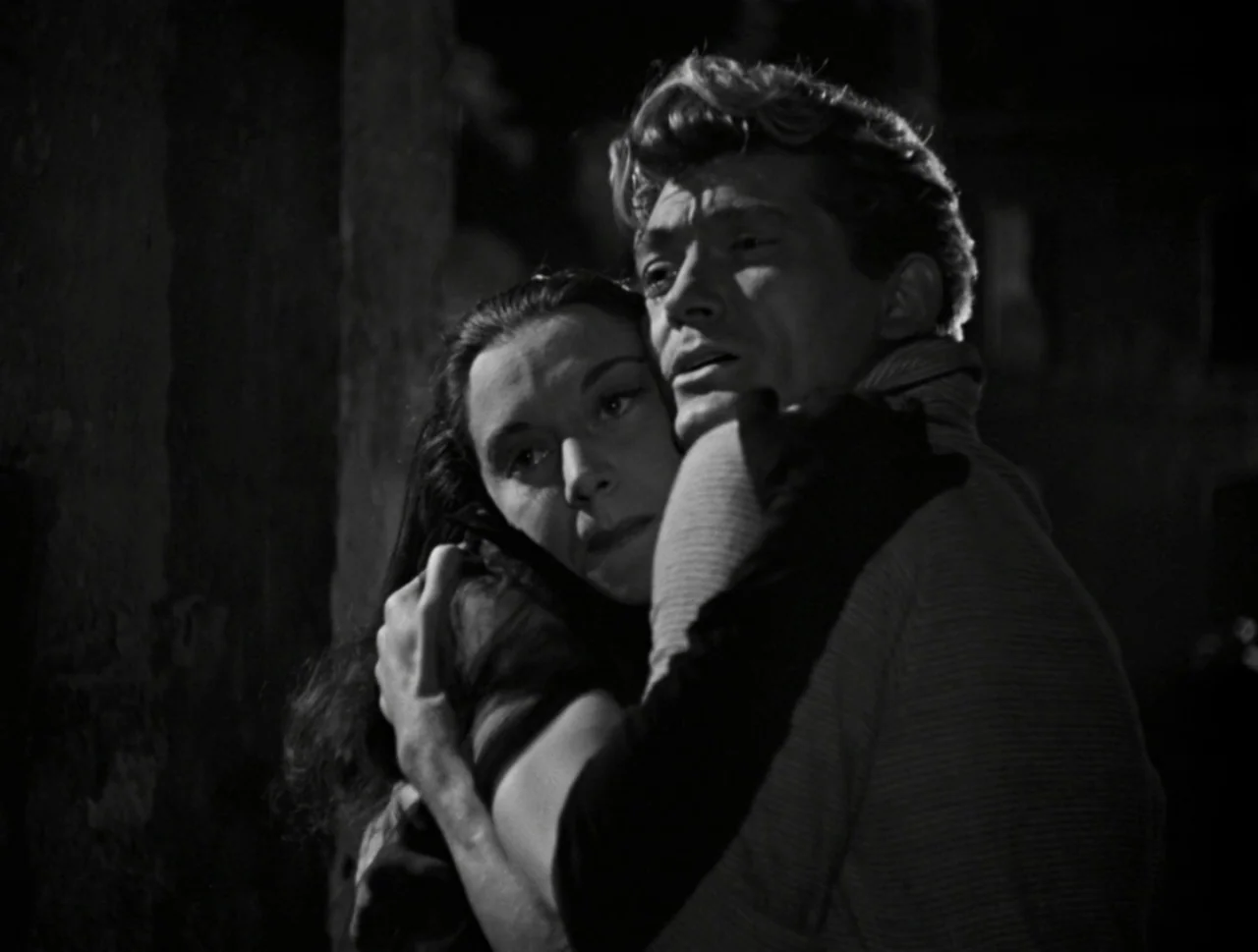 Orpheus (1950) movie still: medium — A dark outdoor space at night with a textured vertical wall in the background. A man and a woman hold each…