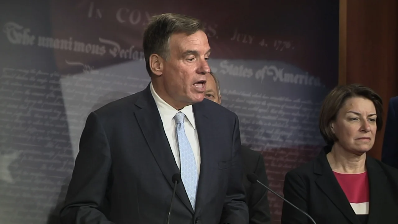 Kill Chain: The Cyber War on America's Elections (2020) movie still: medium — A man and woman stand before a backdrop featuring the US Declaration…