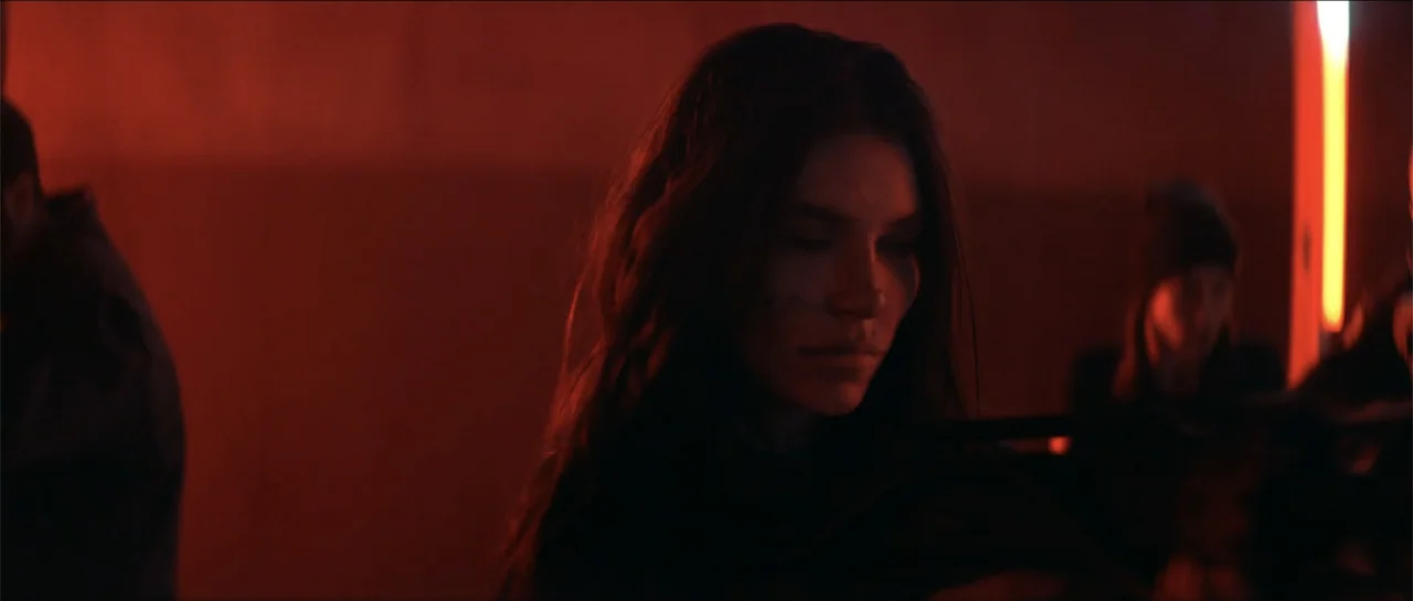 Cosmic Sin (2021) movie still: medium — An interior space bathed in intense red light with a dark, indistinct background. A young woman stands…