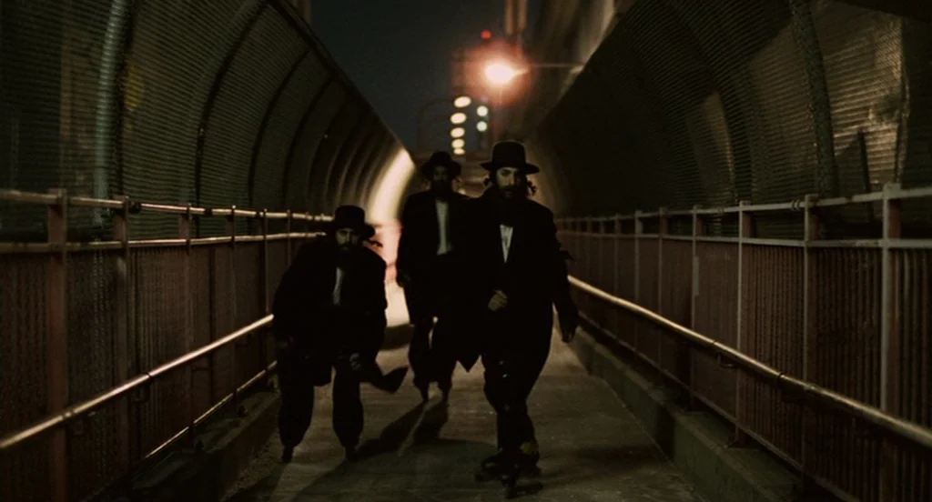 It’s Kind Of A Funny Story (2010) movie still: fullbody — Three men in traditional dark attire run along a metal-fenced outdoor walkway at night. A…