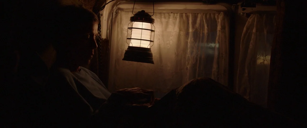 Nomadland (2020) movie still: medium — The interior of a van at night features draped curtains over the rear windows. A person sits in the dark,…