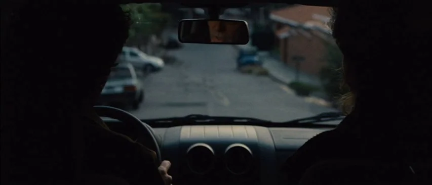 The Headless Woman (2008) movie still: medium — A view from the back seat of a car looking out through the front windshield. A driver and passenger…