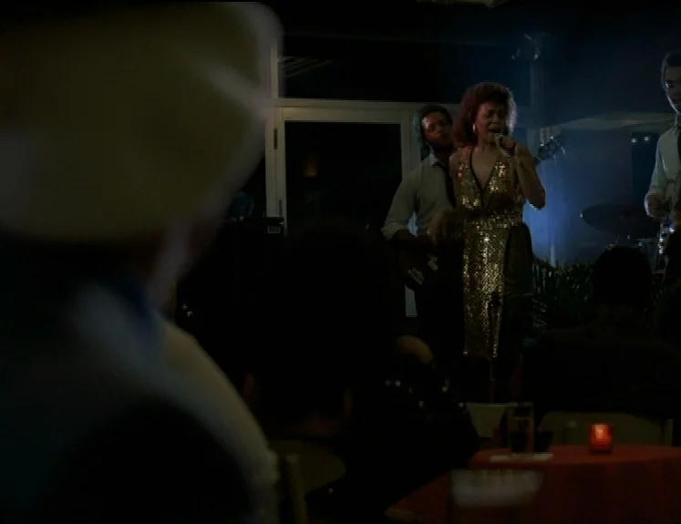 The Brother From Another Planet (1984) movie still: medium — A dimly lit club environment with patrons seated at red tables in the foreground. A…