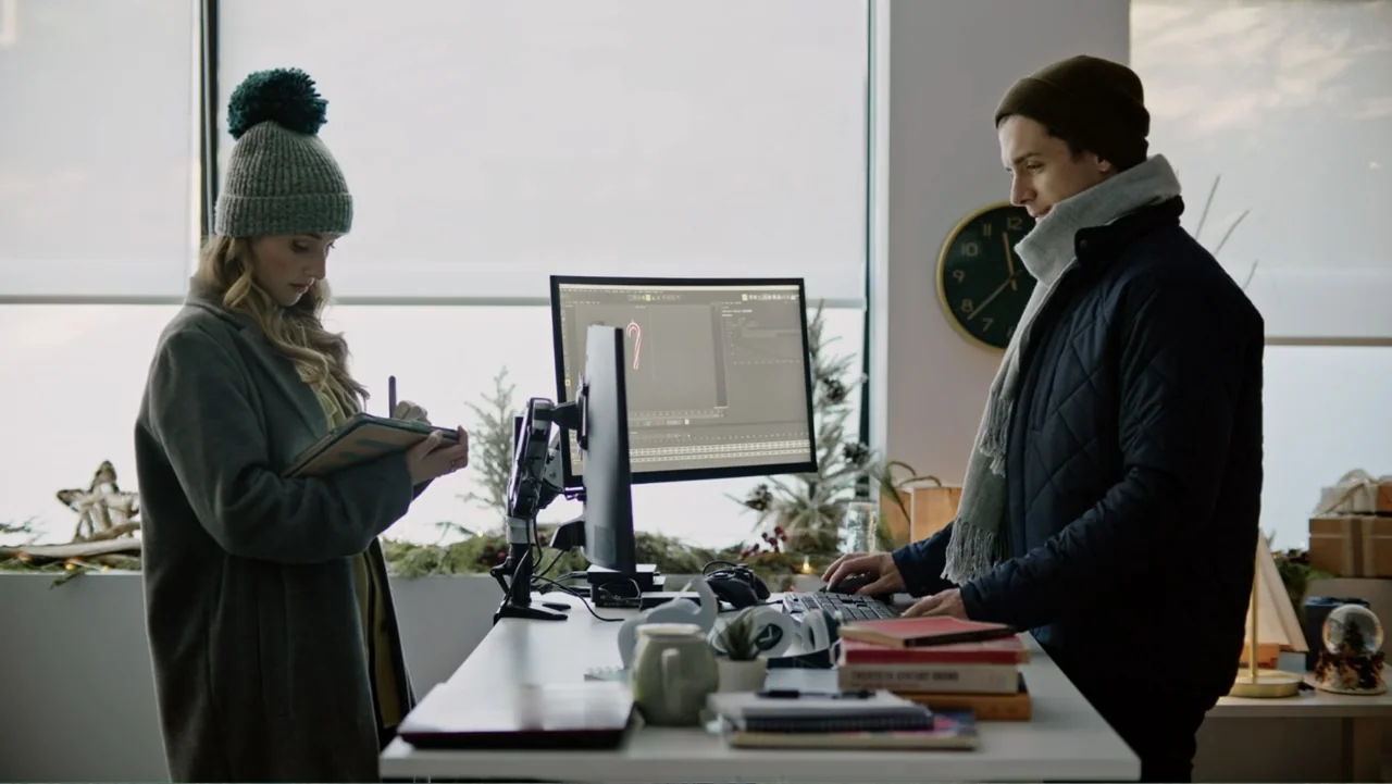 Ghosts of Christmas Past (2021) movie still: medium — A modern workspace with large windows overlooking trees features two people working together…