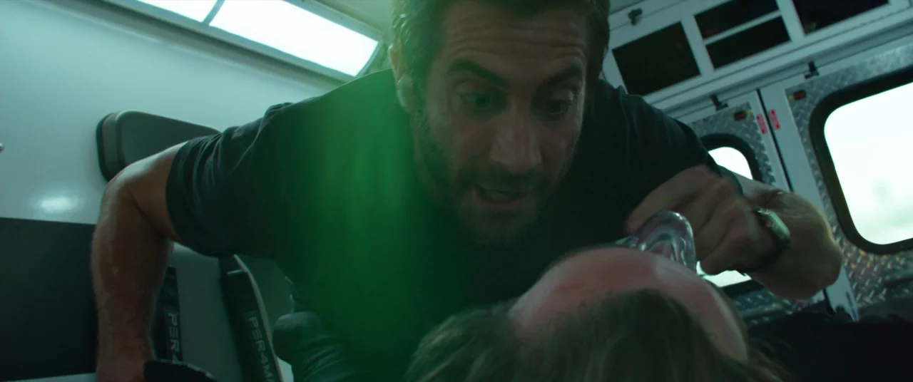 Ambulance (2022) movie still: medium — The interior of a moving ambulance with white walls and metal fittings. A man leans over a supine patient…