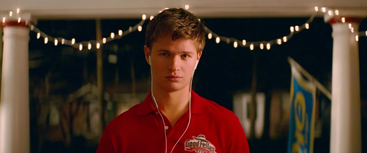 Baby Driver (2017) movie still: medium — A residential porch decorated with glowing string lights at night. A young man stands in the center looking…
