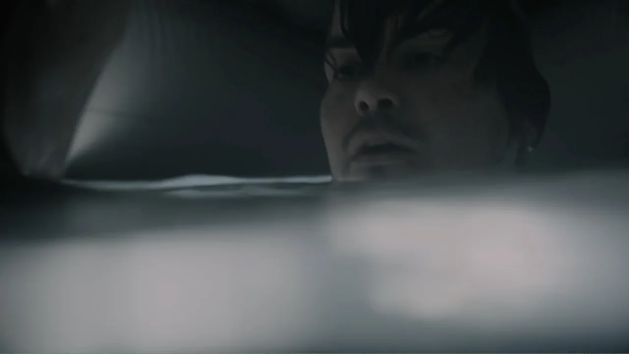 Capsized: Blood in the Water (2019) movie still: closeup — A person is submerged in a tub of dark water inside a dim room. Only the face and hair of…