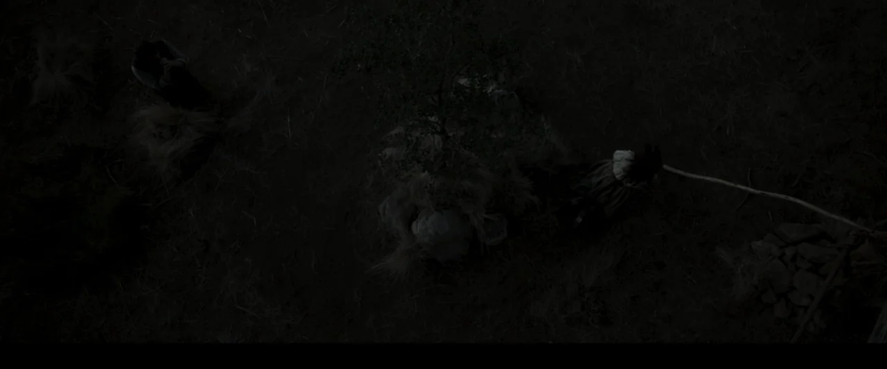 Fatima (2020) movie still: establishing — A dark, expansive open field at night with scattered dry vegetation and small rocks. Two people are…