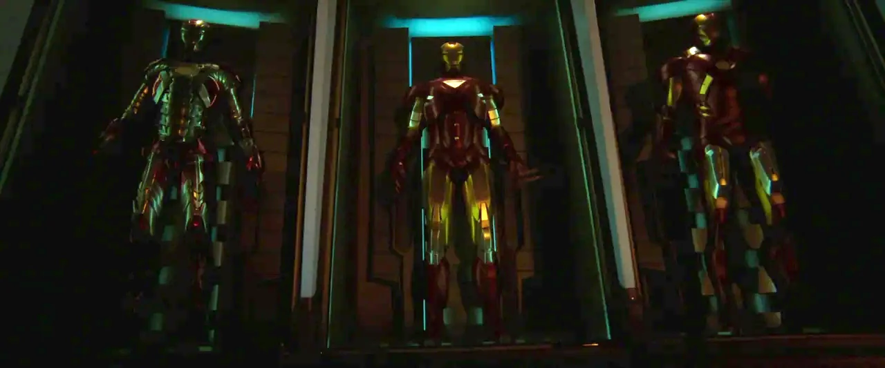 Iron Man 3 (2013) movie still: wide — Three metal suits stand inside separate dark alcoves illuminated by vertical blue light strips. The suits are…