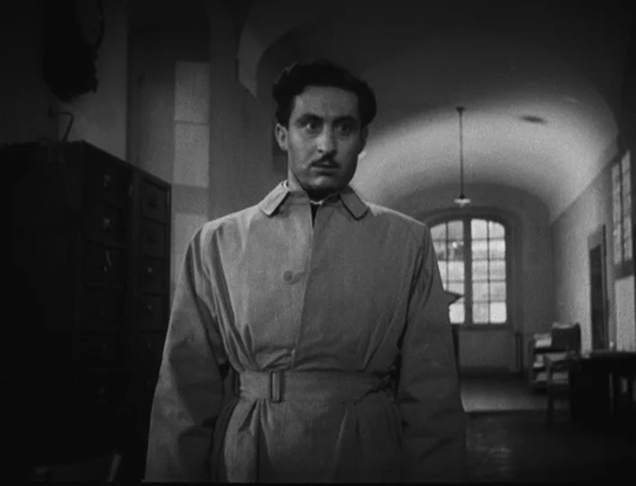 The White Sheik (1952) movie still: medium — A long stone-walled corridor with an arched ceiling and a wooden file cabinet nearby. A man wearing a…