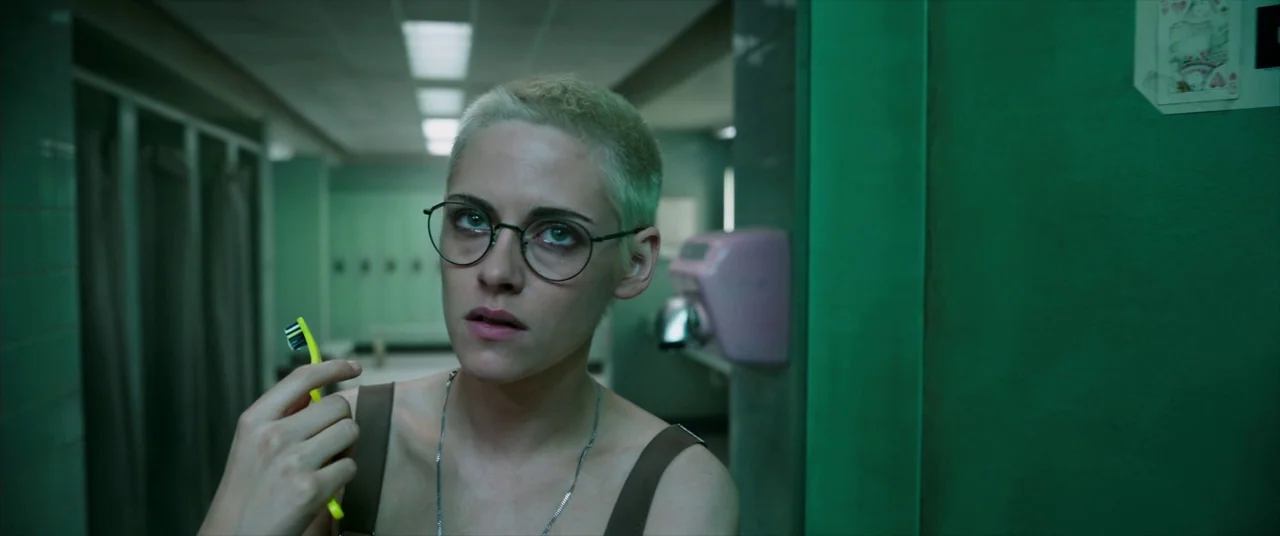 Underwater (2020) movie still: medium — A locker room with rows of metal lockers and green tile walls. A woman with short bleached hair holds a…