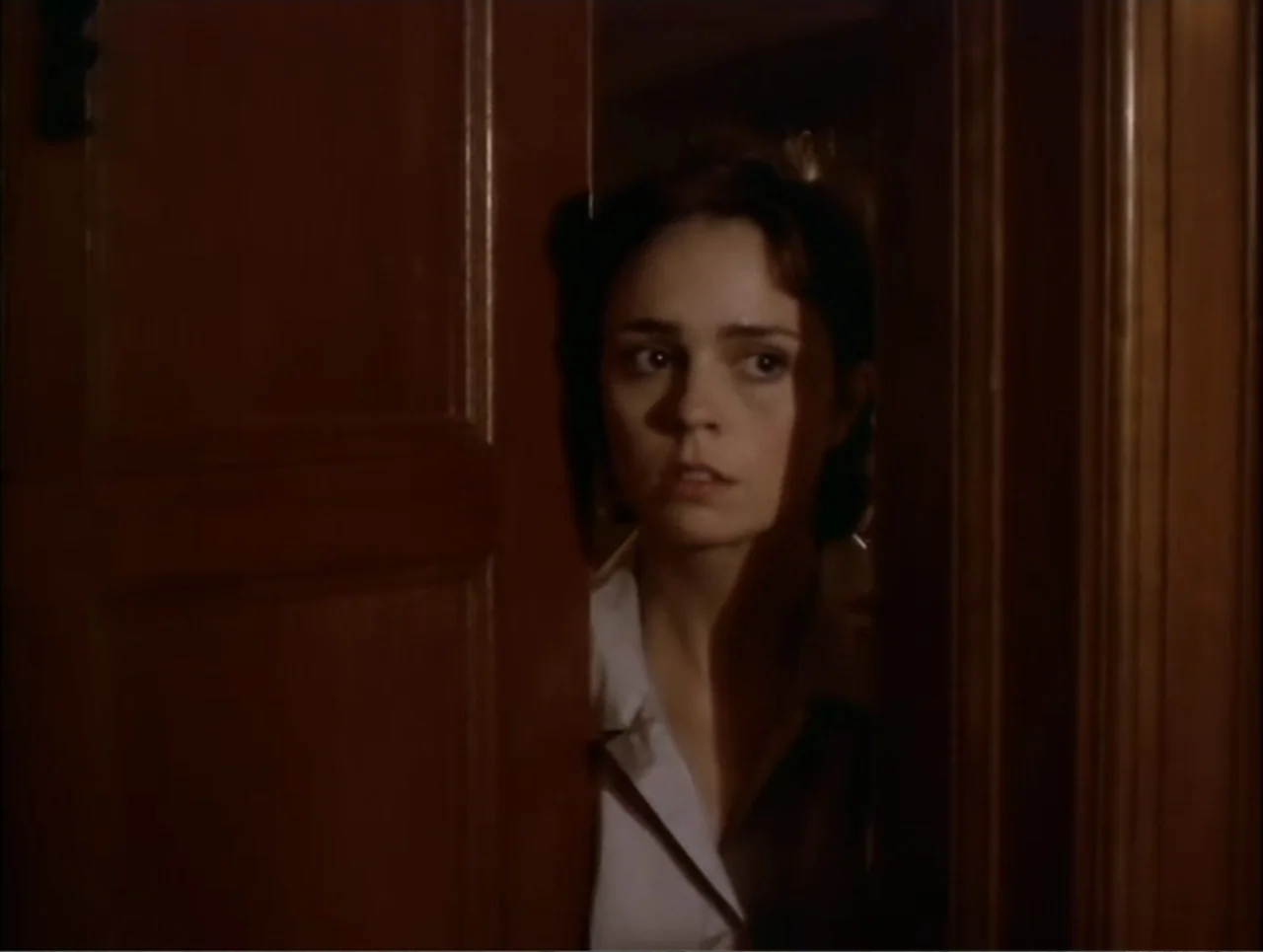At the Midnight Hour (1995) movie still: closeup — A dark wooden door is cracked open revealing a dimly lit room interior. A young woman with dark…