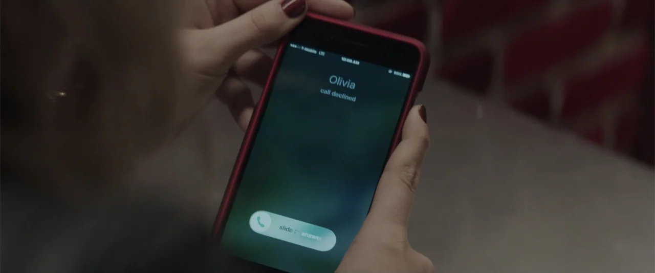 Truth or Dare (2018) movie still: closeup — A close up view shows hands holding a smartphone displaying an incoming call screen. The screen glows…