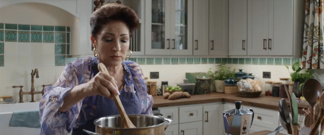 Father of the Bride (1991) movie still: medium — A well-lit residential kitchen features light gray cabinets and a wooden countertop. A woman in a…