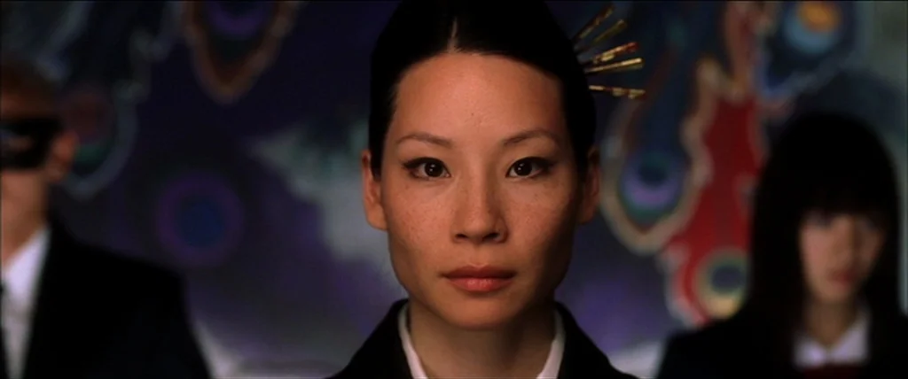 Kill Bill Vol. 1 (2004) movie still: closeup — An interior space features a blurry, stylized wall mural with peacock feather patterns. A woman with…
