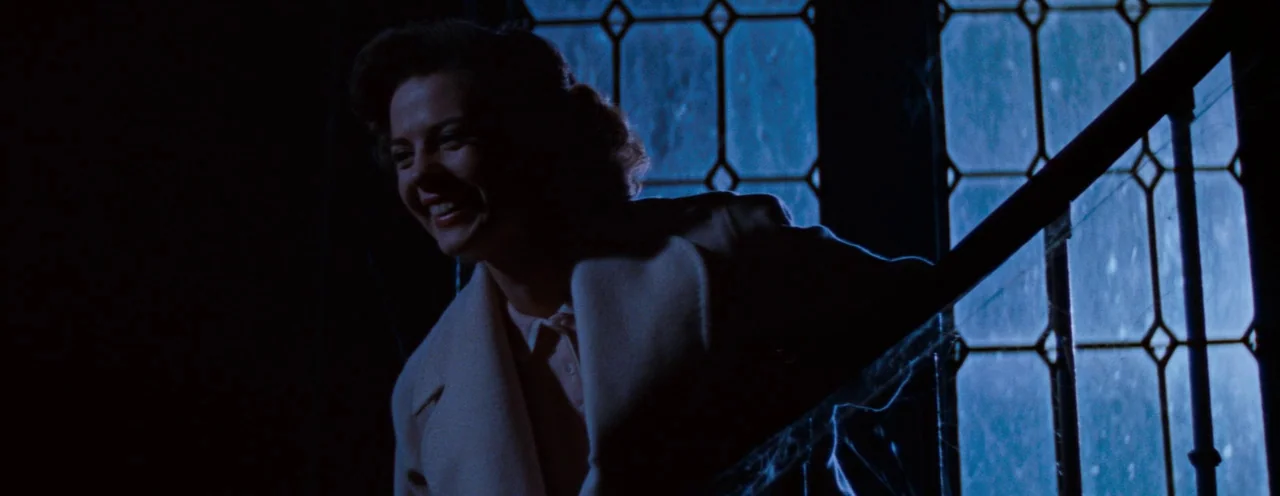 Rebel Without A Cause (1955) movie still: medium — A dark staircase with spiderwebs on a wooden railing is lit by moonlight. A woman in a light coat…