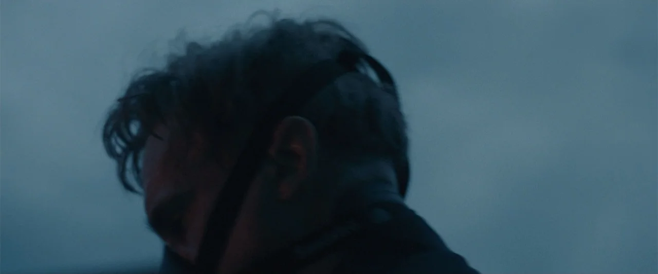 Maggie (2015) movie still: closeup — An outdoor setting under a blue evening sky with a blurry background. A man seen in side profile looks downward…