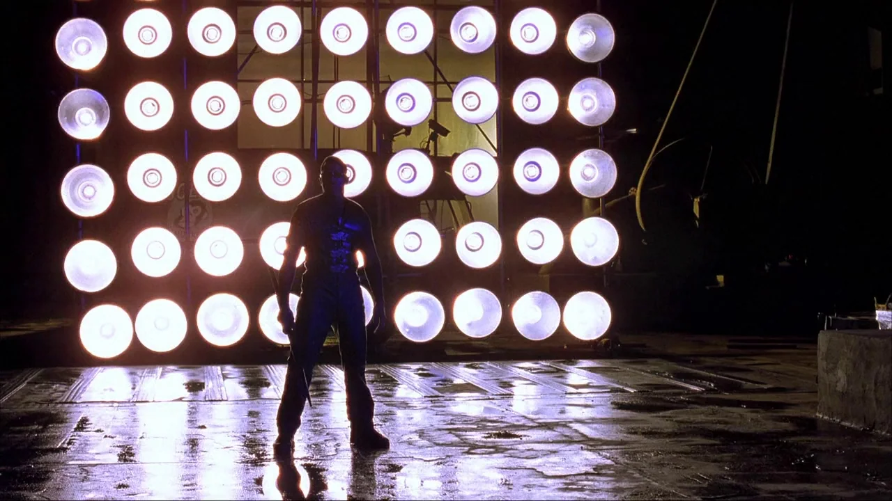 Blade II (2002) movie still: fullbody — A dark outdoor space features a massive panel of circular, bright white stage lights. A single male figure…