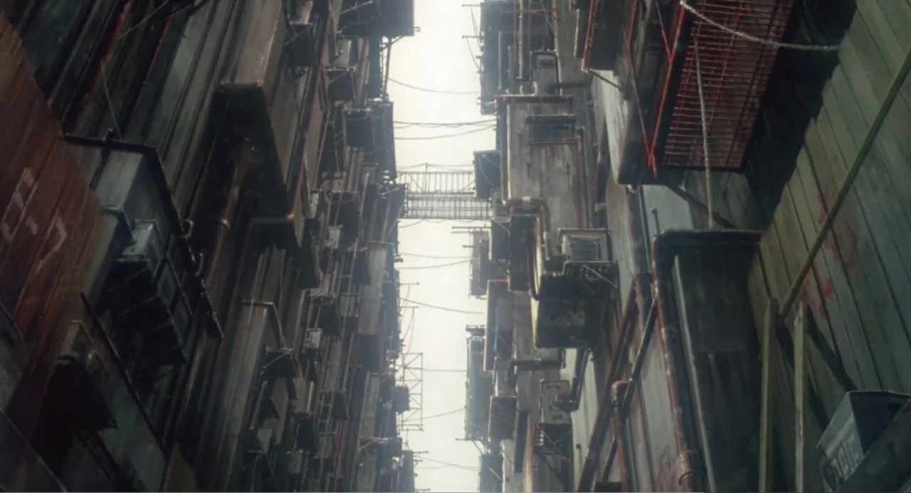 Ghost in the Shell (1995) movie still: establishing — A narrow alleyway sits between two towering, dilapidated apartment buildings covered in pipes.…