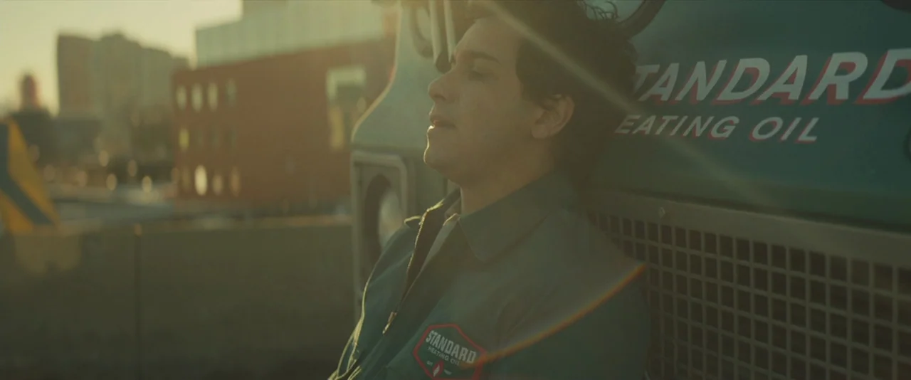 A Most Violent Year (2014) movie still: medium — A man in a green work jacket leans against the front of a delivery truck. The background shows…