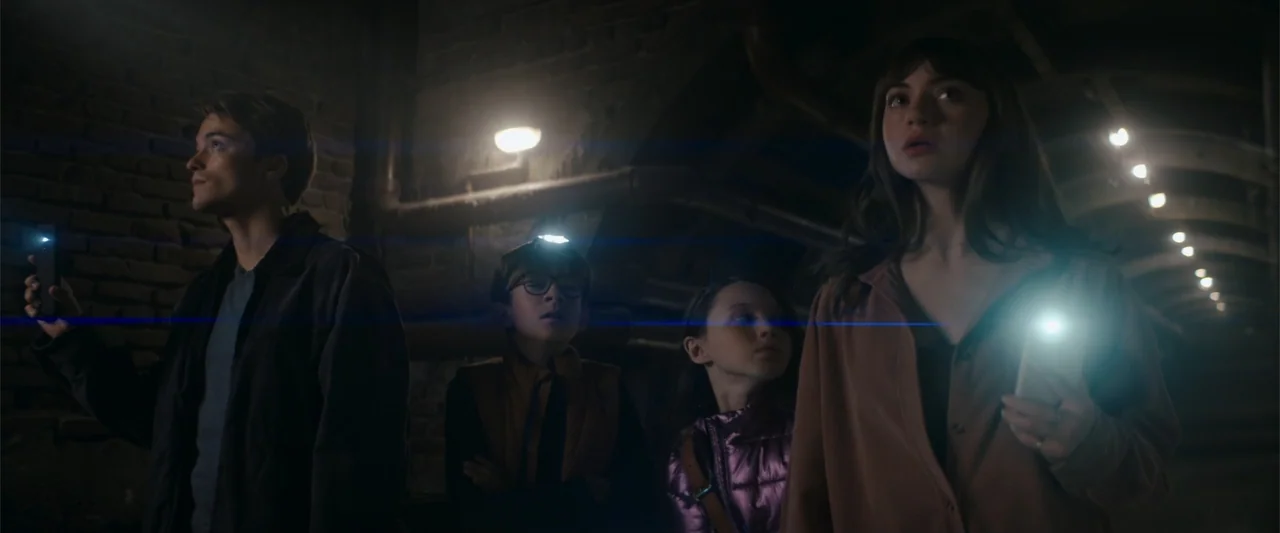 A Christmas Mystery (2022) movie still: medium — A dark brick passage features curved walls and exposed pipes along the ceiling. Four people…