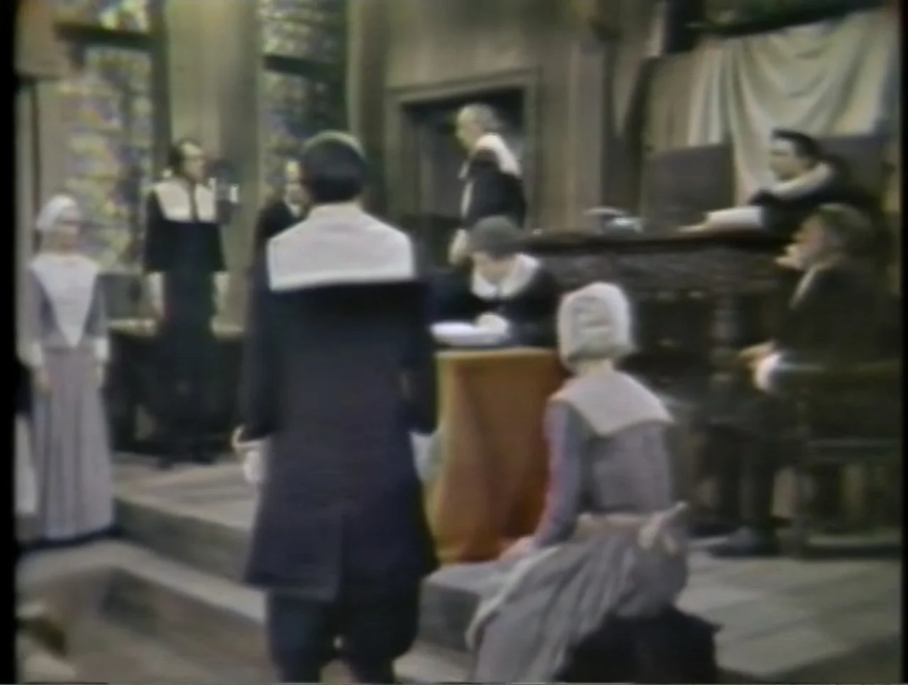 The Crucible (1996) movie still: medium — A austere room with wooden furniture and neutral-toned wall hangings serves as a court. Several people in…