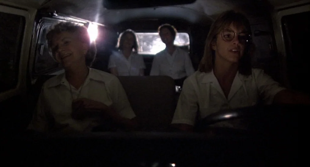 Salvador (1986) movie still: medium — Four women ride inside the back of a dimly lit moving van at night. They sit in rows wearing white shirts…