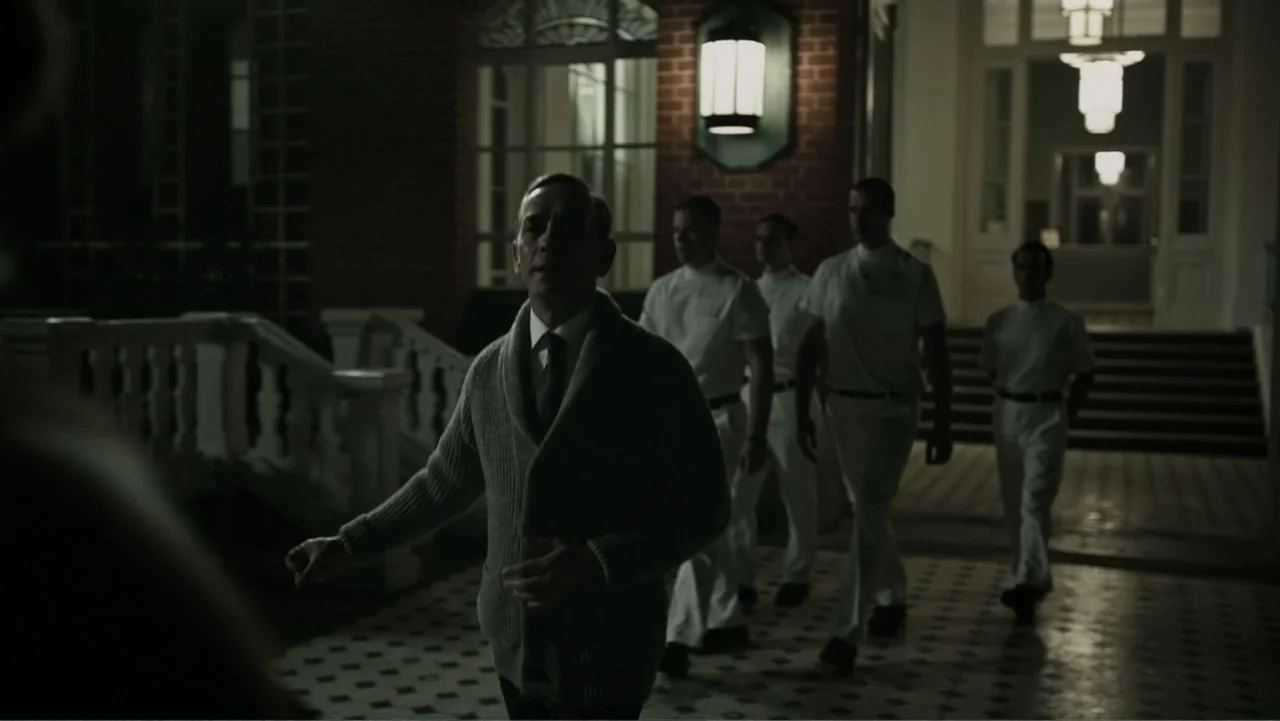 A Cure for Wellness (2017) movie still: medium — A courtyard at night sits before a brick building with illuminated glass doors. An older man in a…