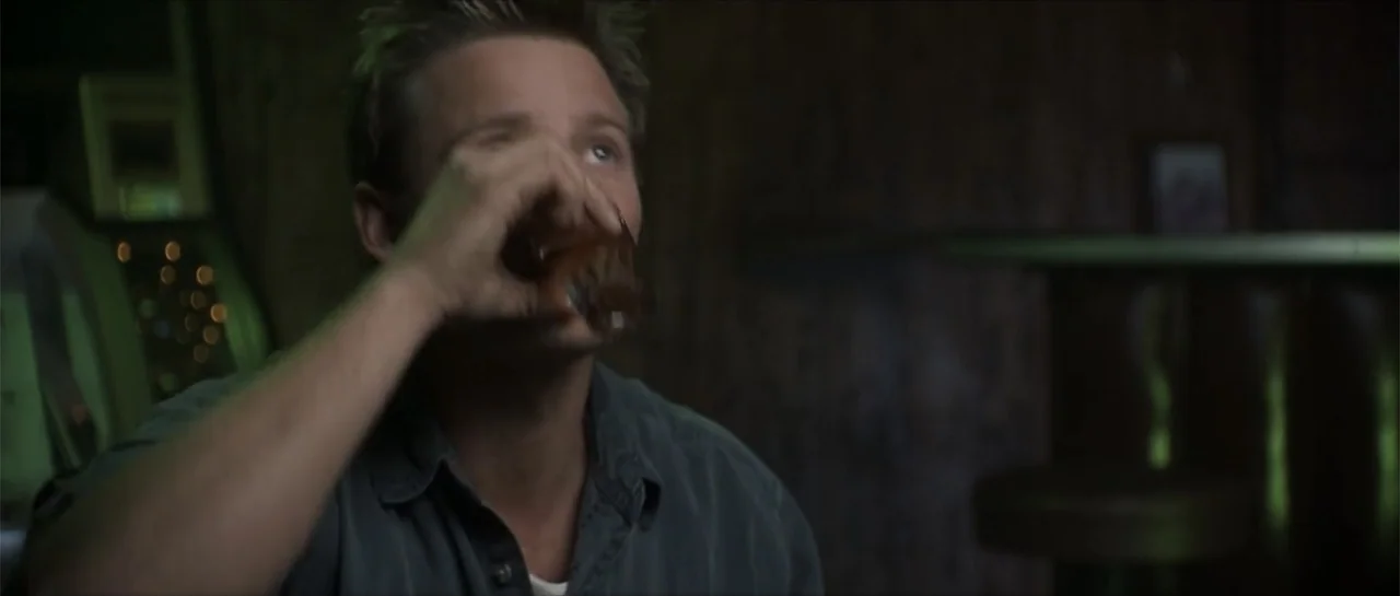 Joy Ride (2001) movie still: medium — A dark, dimly lit bar environment contains wooden surfaces and ambient neon lighting. A man in his thirties…
