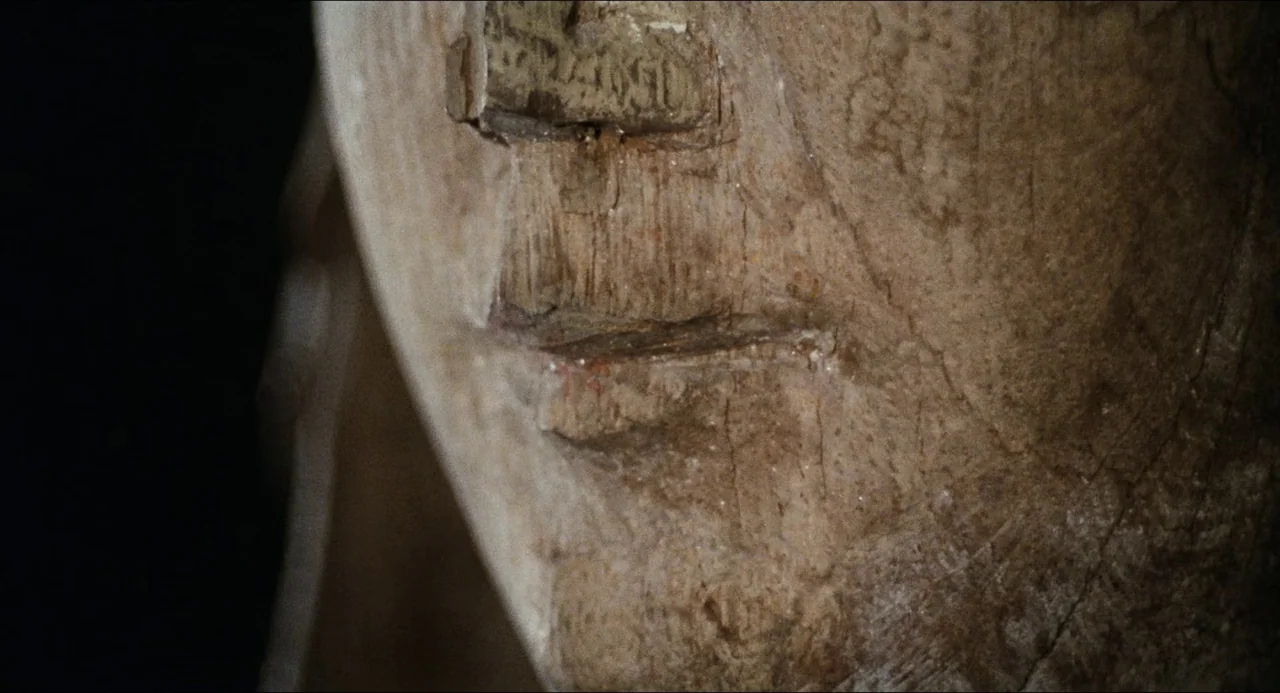 The Touch (1971) movie still: closeup — An ancient stone sculpture fragment displays intricate carved details and worn surfaces. The artifact is…