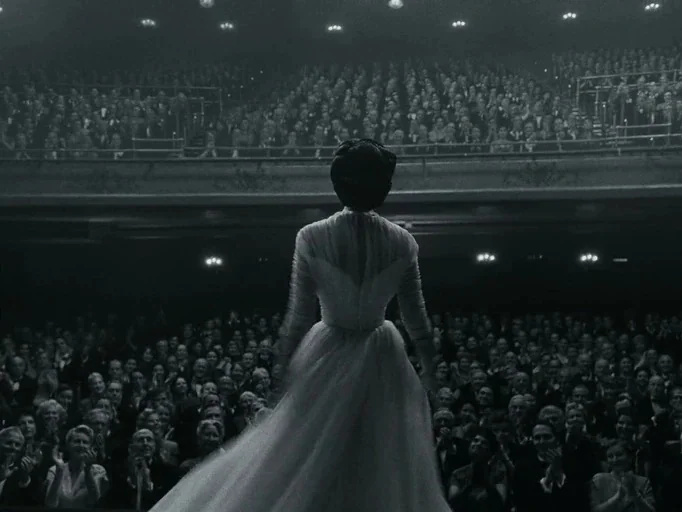 Maestro (2023) movie still: fullbody — A grand concert hall is packed with an audience seated in tiers of balconies. A woman in a flowing white gown…